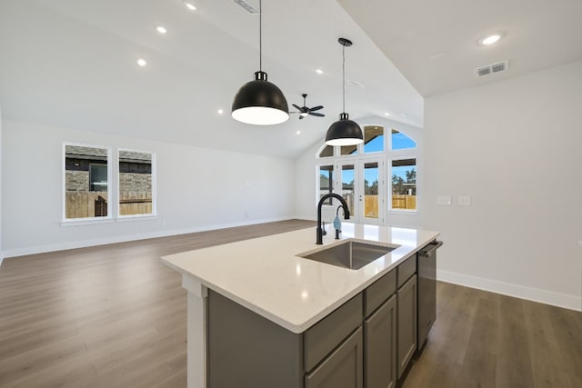 kitchen featuring vaulted ceiling, pendant lighting, sink, light stone countertops, and a center island with sink