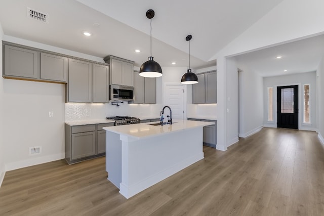 kitchen with lofted ceiling, sink, gray cabinetry, an island with sink, and stove