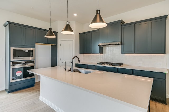 8508 Dongan Dr, Austin, TX 78744 - kitchen featuring stainless steel appliances, a kitchen island with sink, decorative backsplash, light wood-style flooring, and light countertops