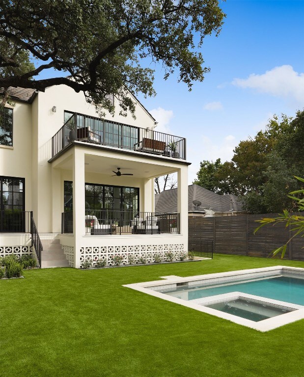 rear view of property featuring a pool with hot tub, a lawn, a patio, a balcony, and ceiling fan