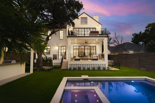 back house at dusk featuring ceiling fan, a fenced in pool, a patio area, a balcony, and a lawn