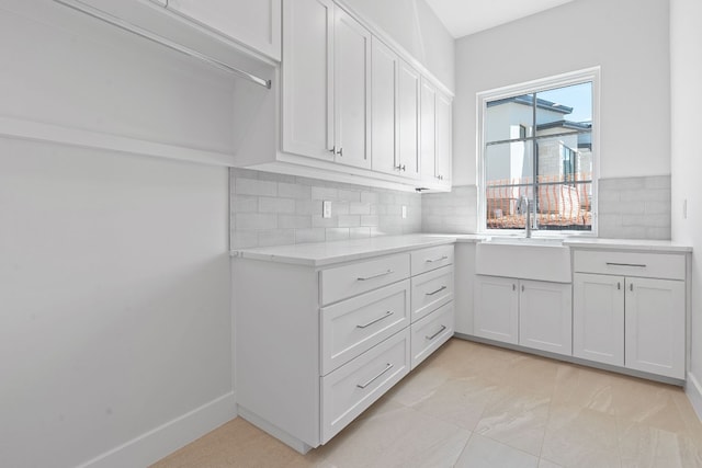 kitchen featuring decorative backsplash, white cabinetry, light tile patterned floors, and sink