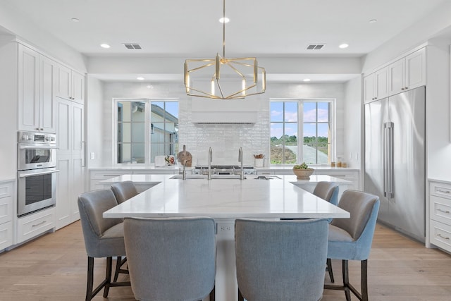 kitchen with a kitchen island with sink, white cabinets, a kitchen bar, light hardwood / wood-style flooring, and appliances with stainless steel finishes