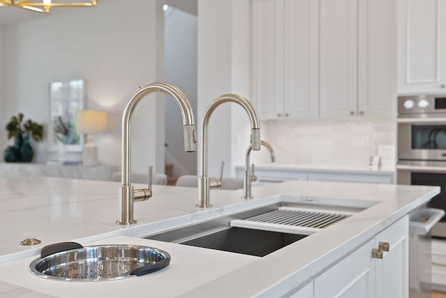 details with light stone counters, sink, white cabinetry, double oven, and decorative backsplash