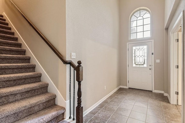 entrance foyer with baseboards, a high ceiling, stairs, and tile patterned floors