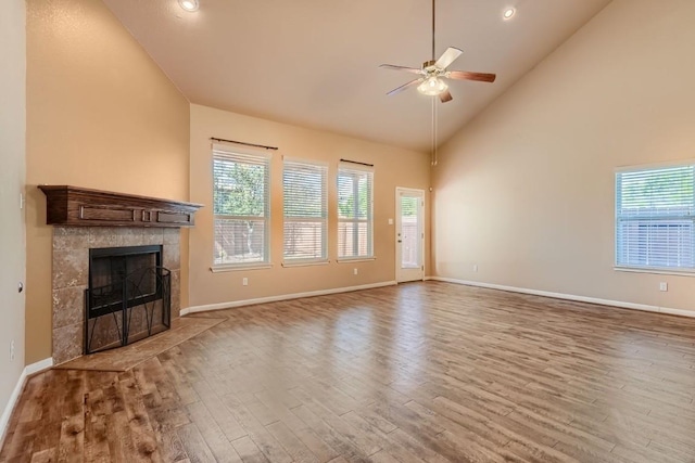 unfurnished living room with high vaulted ceiling, wood finished floors, plenty of natural light, and a tile fireplace