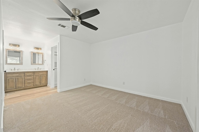 unfurnished bedroom with ceiling fan, light colored carpet, connected bathroom, and sink