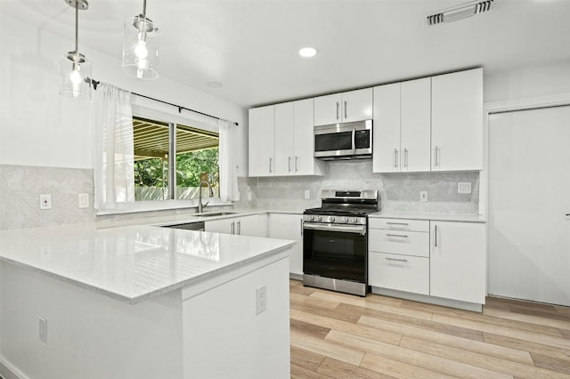 kitchen with white cabinets, kitchen peninsula, stainless steel appliances, light hardwood / wood-style flooring, and decorative light fixtures