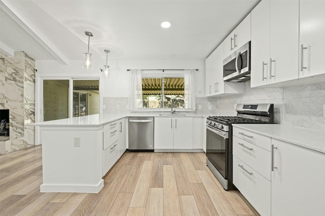 kitchen featuring hanging light fixtures, kitchen peninsula, stainless steel appliances, and white cabinets