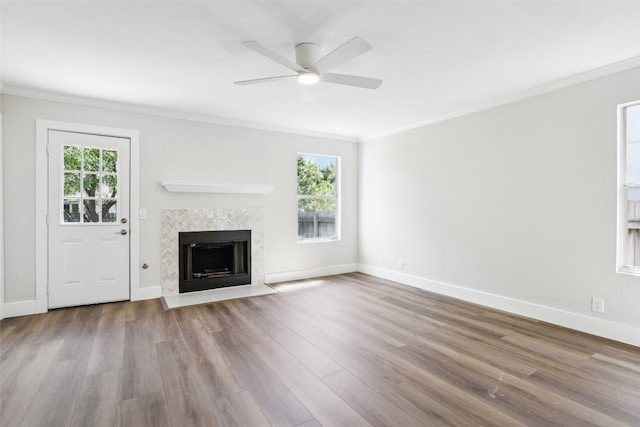 unfurnished living room featuring a healthy amount of sunlight, crown molding, a tiled fireplace, and light hardwood / wood-style flooring