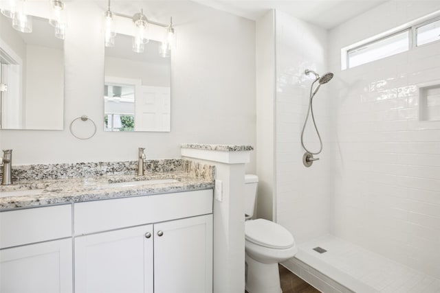 bathroom featuring a tile shower, hardwood / wood-style floors, vanity, and toilet