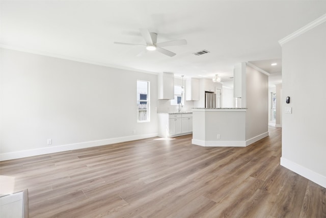 unfurnished living room featuring light wood-type flooring, ceiling fan, sink, and crown molding