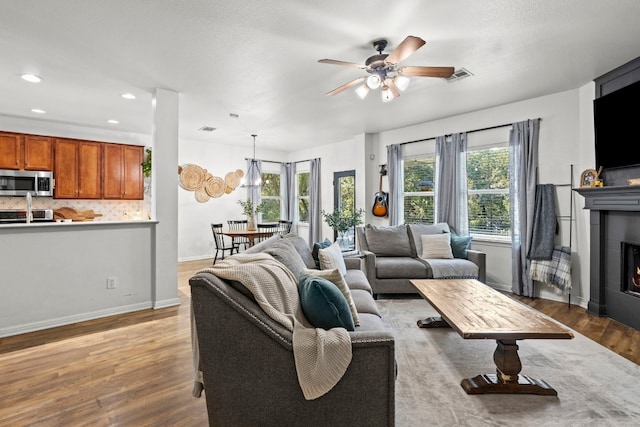 living room with ceiling fan, a tile fireplace, and light hardwood / wood-style flooring