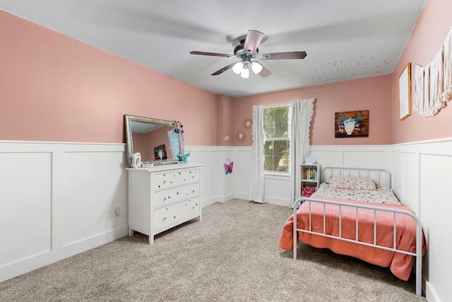 bedroom featuring a wainscoted wall, ceiling fan, and light carpet