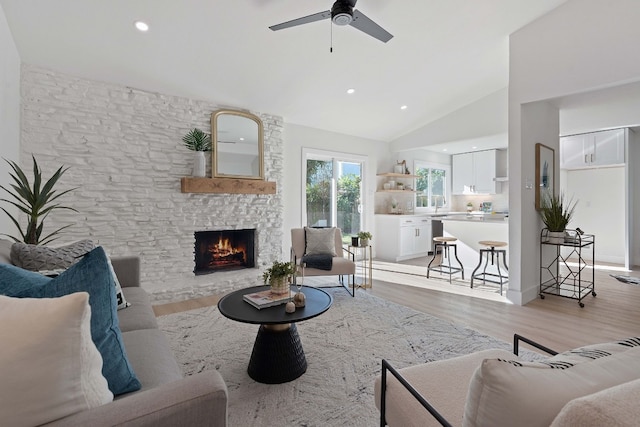 living room featuring a stone fireplace, light hardwood / wood-style floors, ceiling fan, and high vaulted ceiling