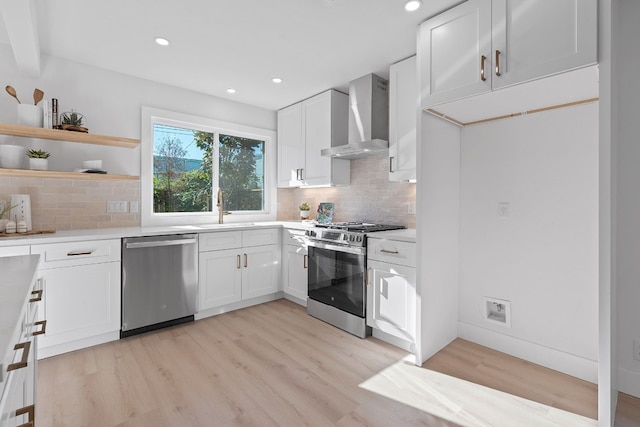 kitchen with appliances with stainless steel finishes, white cabinets, wall chimney exhaust hood, light wood-type flooring, and sink