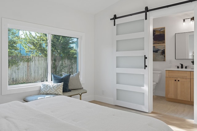 bedroom featuring light hardwood / wood-style floors, sink, vaulted ceiling, a barn door, and ensuite bathroom