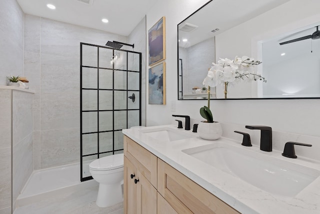 bathroom with a tile shower, ceiling fan, vanity, and toilet