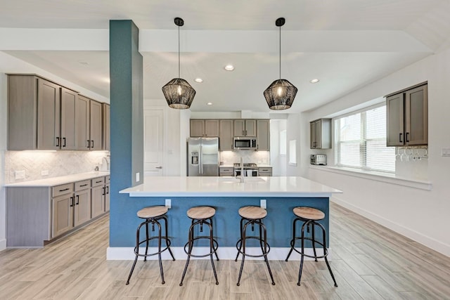 kitchen with backsplash, light hardwood / wood-style floors, pendant lighting, and stainless steel appliances