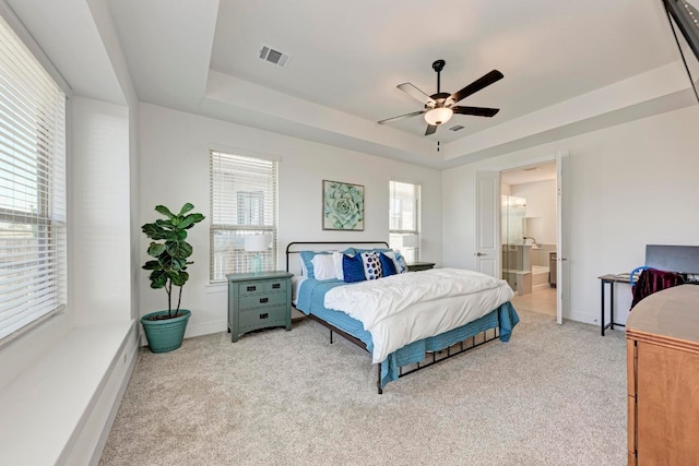 carpeted bedroom with ceiling fan, a raised ceiling, and ensuite bath