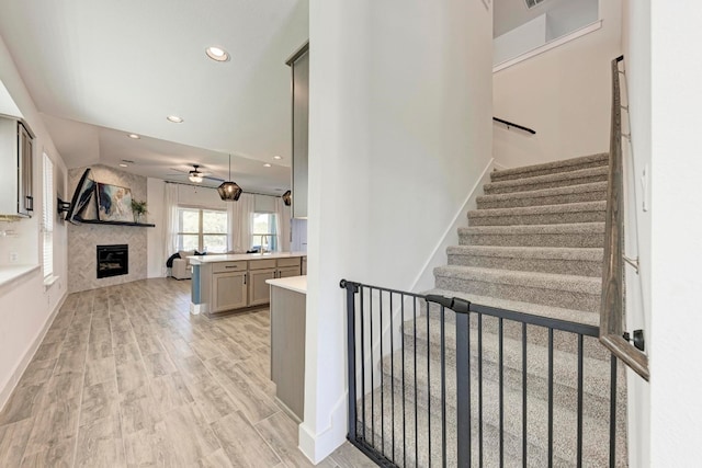 stairs with ceiling fan, hardwood / wood-style flooring, and a tiled fireplace