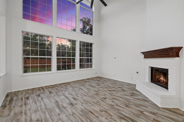 unfurnished living room featuring a brick fireplace, a high ceiling, wood-type flooring, and ceiling fan