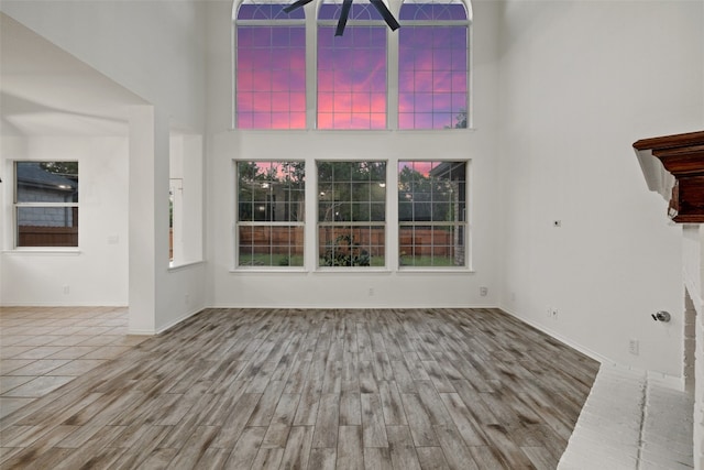 unfurnished living room with ceiling fan, a towering ceiling, and light wood-type flooring