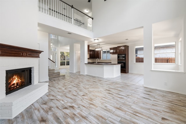 unfurnished living room with a brick fireplace, light hardwood / wood-style floors, a high ceiling, and sink