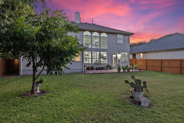 back house at dusk with a patio area and a yard