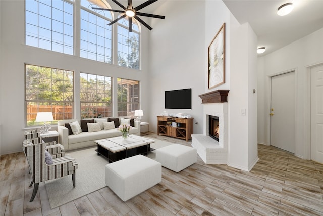 living room featuring ceiling fan, a brick fireplace, and a high ceiling