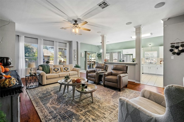 living area with visible vents, light wood finished floors, a ceiling fan, and decorative columns