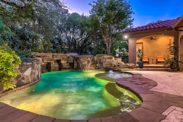 pool at dusk with ceiling fan and a patio area