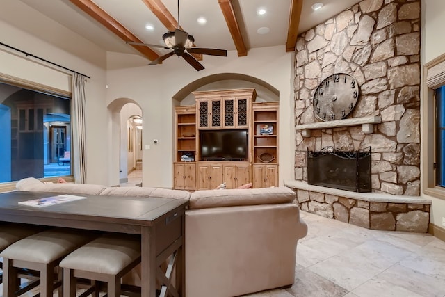 living room with ceiling fan, beamed ceiling, and a fireplace