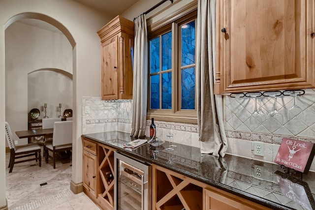 bar featuring beverage cooler, backsplash, and dark stone countertops