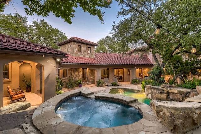 back house at dusk with a swimming pool with hot tub, a patio, and pool water feature