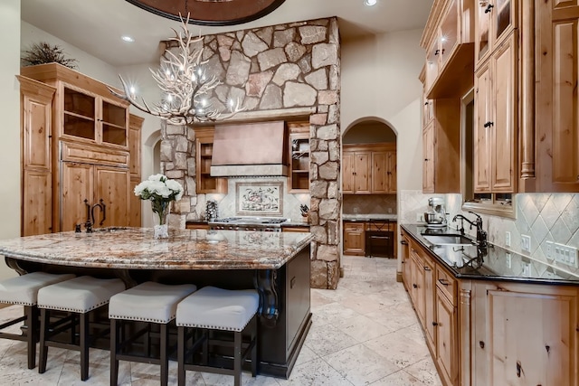 kitchen featuring wall chimney range hood, pendant lighting, dark stone countertops, sink, and a spacious island