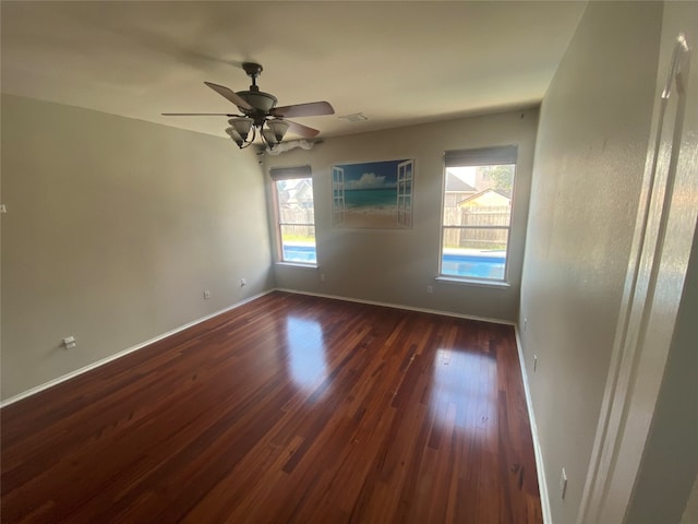 empty room featuring ceiling fan, dark wood-type flooring, and a wealth of natural light