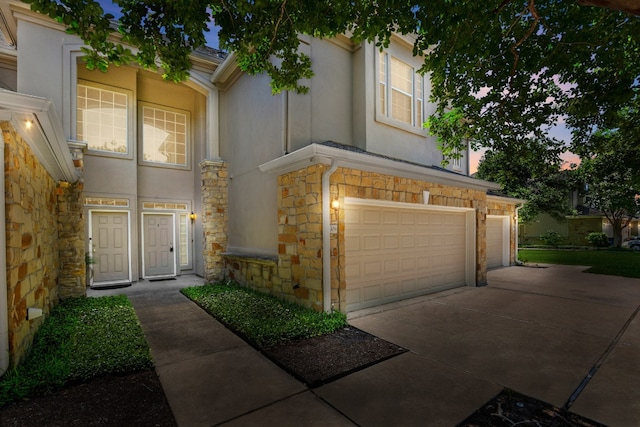 view of front of house featuring stone siding, an attached garage, driveway, and stucco siding