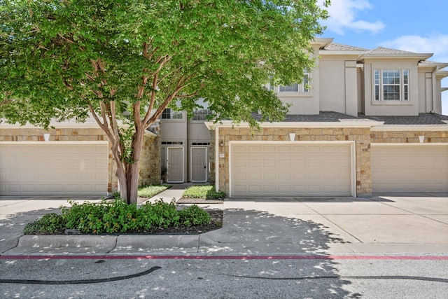 multi unit property with stone siding, driveway, an attached garage, and stucco siding