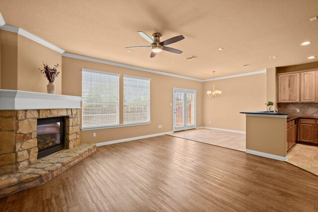 living room with ceiling fan with notable chandelier, light hardwood / wood-style floors, a stone fireplace, and crown molding