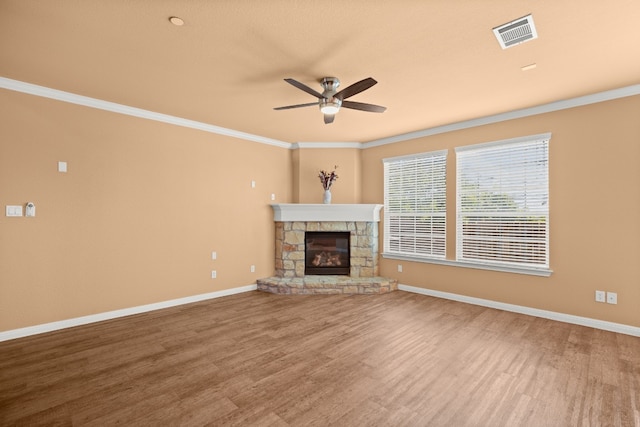 unfurnished living room with hardwood / wood-style floors, ceiling fan, a stone fireplace, and ornamental molding