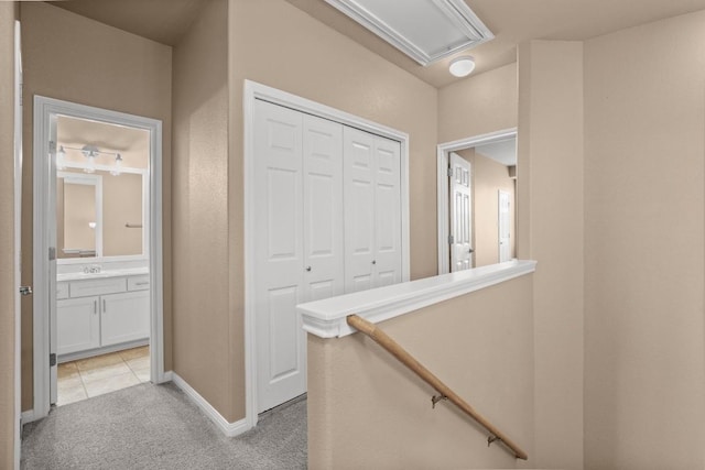 hall with baseboards, an upstairs landing, and light colored carpet