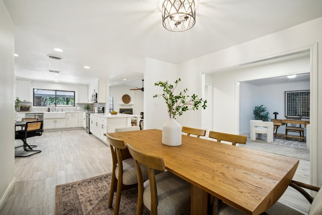 dining area featuring ceiling fan with notable chandelier, light wood-type flooring, and sink