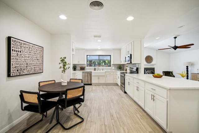 kitchen with sink, backsplash, white cabinetry, stainless steel appliances, and light hardwood / wood-style floors