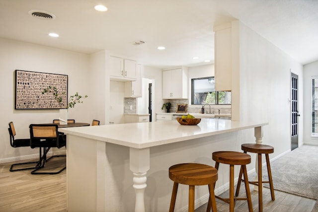 kitchen with light wood-type flooring, a breakfast bar, white cabinetry, and tasteful backsplash