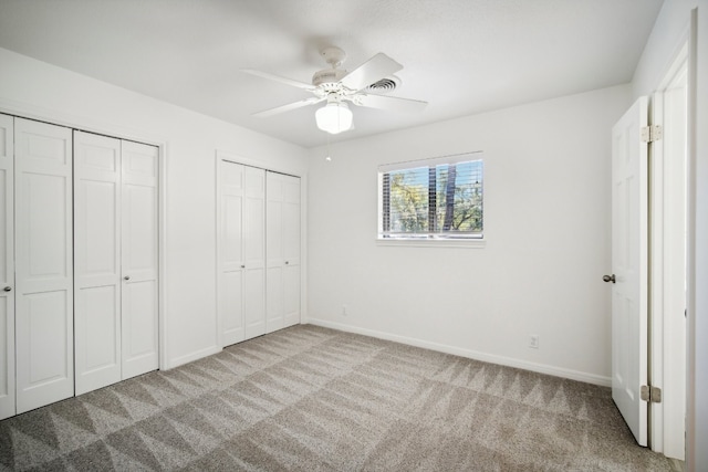 unfurnished bedroom featuring multiple closets, ceiling fan, and light colored carpet