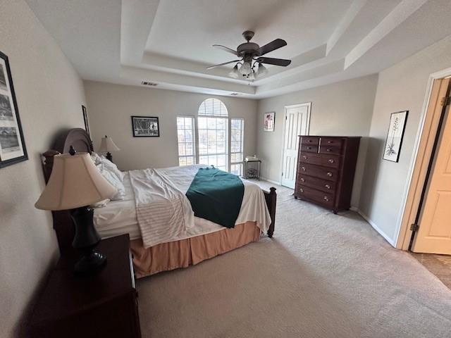 carpeted bedroom featuring ceiling fan and a tray ceiling