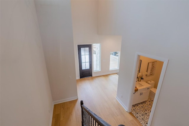 foyer entrance with light wood-style flooring, a towering ceiling, and baseboards
