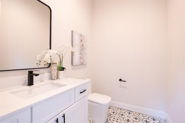 half bath featuring toilet, tile patterned floors, vanity, and baseboards