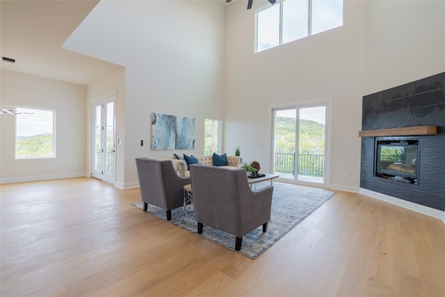 living room with ceiling fan, a fireplace, a towering ceiling, and light hardwood / wood-style floors